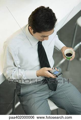 Stock Photograph - Executive holding cup of coffee and checking cell phone. Fotosearch