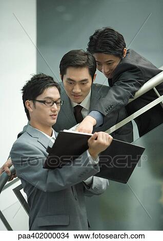 Three business executives looking at agenda together View Large Photo Image Picture - Three business executives looking at agenda together. Fotosearch