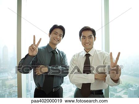 Two businessmen making victory sign, smiling at camera View Large Photo Image Stock Photo - Two businessmen making victory sign, smiling at camera. Fotosearch