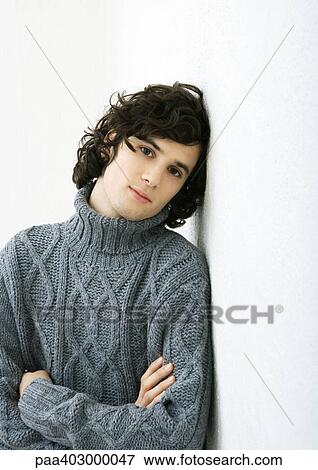 Stock Photo - Young man leaning against wall, arms folded, portrait. Fotosearch