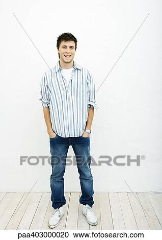 Stock Image - Young man standing with hands in pockets, full length portrait. Fotosearch