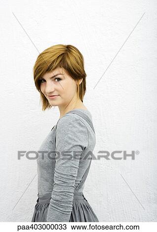 Stock Image - Young woman looking over shoulder at camera, portrait. Fotosearch