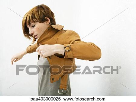 Stock Photograph - Young woman putting on jacket. Fotosearch