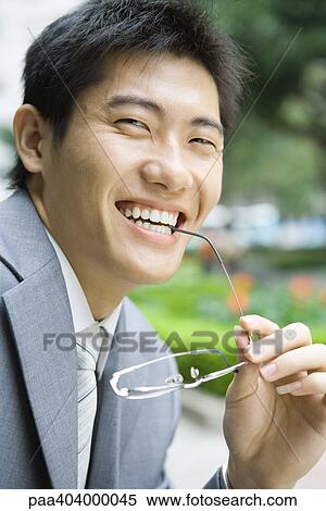Businessman holding glasses up to mouth, smiling at camera, portrait View Large Photo Image Stock Photography - Businessman holding glasses up to mouth, smiling at camera, portrait. Fotosearch