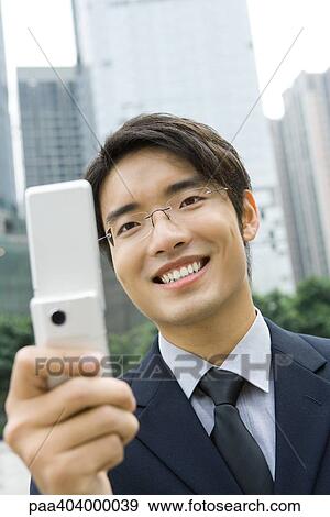 Businessman holding up cell phone, smiling View Large Photo Image Stock Photo - Businessman holding up cell phone, smiling. Fotosearch