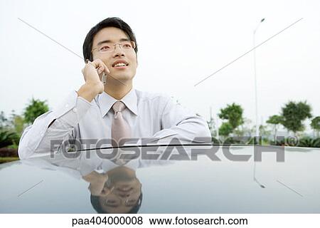 Businessman leaning against car, using cell phone View Large Photo Image Stock Photo - Businessman leaning against car, using cell phone. Fotosearch