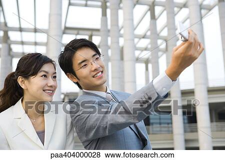 Businessman standing next to female colleague, taking photo with cell phone View Large Photo Image Stock Photo - Businessman standing next to female colleague, taking photo with cell phone. Fotosearch