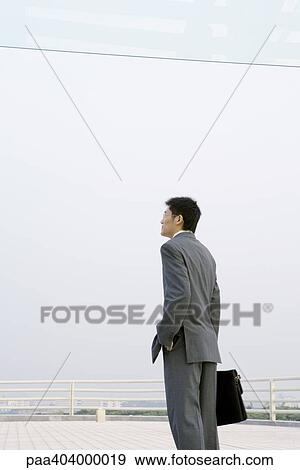 Businessman standing with briefcase, on office building terrace View Large Photo Image Stock Photo - Businessman standing with briefcase, on office building terrace. Fotosearch