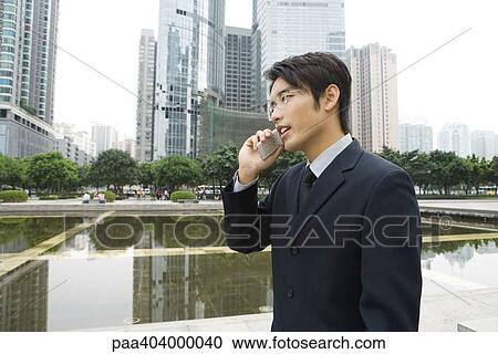 Businessman using cell phone in office park, side view View Large Photo Image Stock Image - Businessman using cell phone in office park, side view. Fotosearch