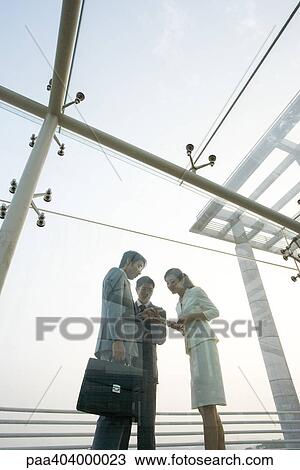 Stock Image - Three young executives talking in covered walkway, low angle view. Fotosearch