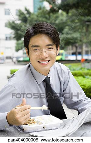 Young businessman eating takeout food outdoors View Large Photo Image Stock Photography - Young businessman eating takeout food outdoors. Fotosearch