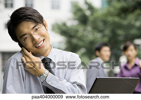 Young businessman holding cell phone against shoulder, smiling at camera View Large Photo Image Stock Photo - Young businessman holding cell phone against shoulder, smiling at camera. Fotosearch
