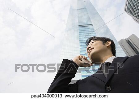 Young businessman using cell phone, skyscraper in background, low angle view View Large Photo Image Stock Image - Young businessman using cell phone, skyscraper in background, low angle view. Fotosearch