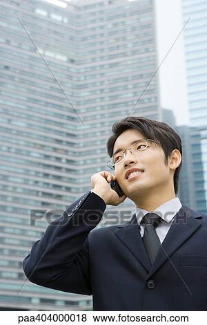 Young businessman using cell phone, looking away, office building in background View Large Photo Image Stock Photo - Young businessman using cell phone, looking away, office building in background. Fotosearch