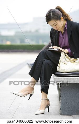 Young businesswoman sitting on bench looking down at cell phone View Large Photo Image Stock Image - Young businesswoman sitting on bench looking down at cell phone. Fotosearch