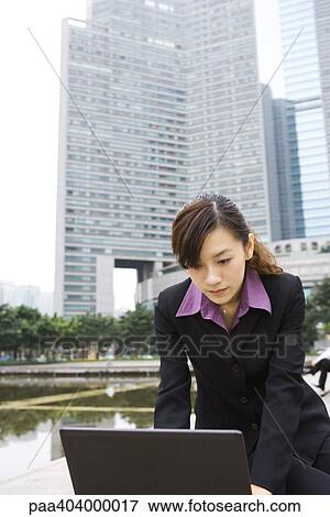 Stock Photo - Young businesswoman using laptop in office park. Fotosearch