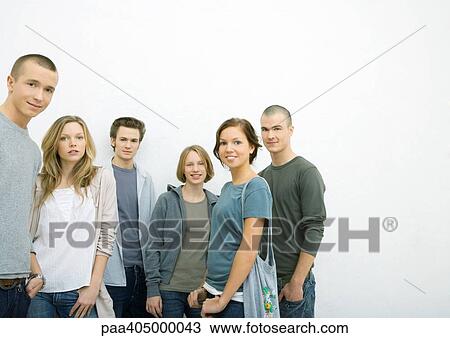 Stock Image - Group of young adults standing with hands in pockets, smiling at camera. Fotosearch
