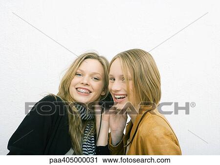 Stock Image - Two young female friends sharing headphones, smiling at camera. Fotosearch