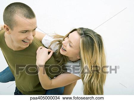 Young couple, man holding young woman on back, looking over shoulder, smiling at each other View Large Photo Image Picture - Young couple, man holding young woman on back, looking over shoulder, smiling at each other. Fotosearch