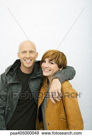 Stock Photo - Young couple, man with arm around woman's shoulders, both smiling at camera. Fotosearch