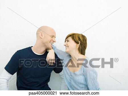 Stock Image - Young couple smiling at each other, face to face, woman with elbow on man's shoulder. Fotosearch