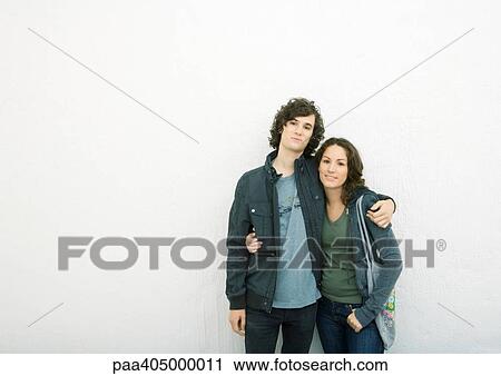 Young couple standing with arms around each other, looking at camera View Large Photo Image Stock Image - Young couple standing with arms around each other, looking at camera. Fotosearch