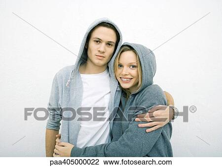 Young couple standing with arms around each other, wearing hooded sweatshirts, looking at camera View Large Photo Image Stock Image - Young couple standing with arms around each other, wearing hooded sweatshirts, looking at camera. Fotosearch