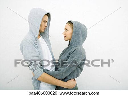 Young couple wearing hooded sweatshirts, holding each other around waist, face to face View Large Photo Image Stock Image - Young couple wearing hooded sweatshirts, holding each other around waist, face to face. Fotosearch