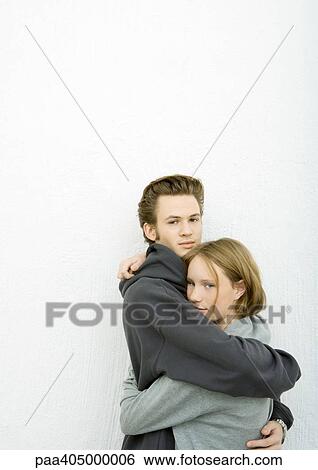 Stock Photograph - Young man and woman hugging, looking at camera. Fotosearch