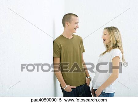 Young man and woman smiling at each other, hands in pockets View Large Photo Image Stock Photography - Young man and woman smiling at each other, hands in pockets. Fotosearch