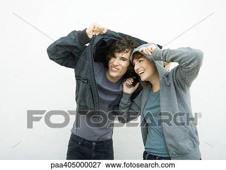Stock Photo - Young man and young woman standing, covering heads with jackets, laughing. Fotosearch