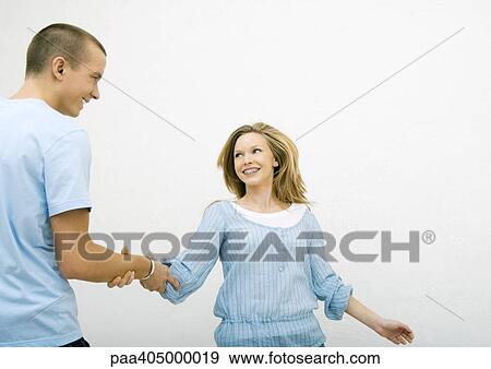 Stock Photo - Young man taking young woman by the arm, both smiling. Fotosearch