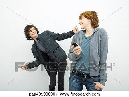 Stock Photo - Young woman holding cell phone, looking over shoulder at male friend dancing behind her . Fotosearch