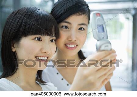 Stock Photograph - Two young female friends looking at cell phone together, close-up. Fotosearch