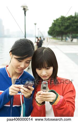 Picture - Two young women using cell phones. Fotosearch