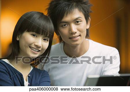 Stock Photo - Young couple smiling at camera, head and shoulders, portrait. Fotosearch