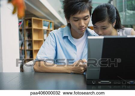Stock Image - Young couple using laptop in library. Fotosearch
