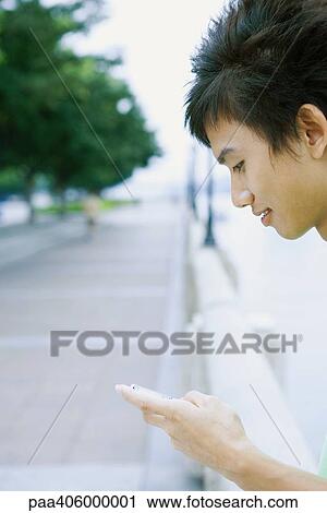 Stock Image - Young man using cell phone, cropped view of head and hand. Fotosearch