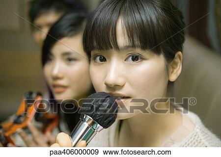 Stock Photo - Young woman holding microphone in karaoke bar, close-up, friends in background. Fotosearch