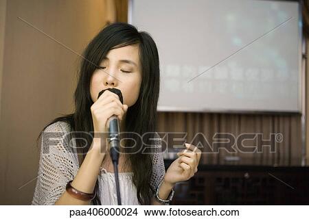 Picture - Young woman singing karaoke, eyes closed. Fotosearch