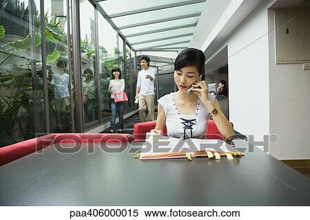Young woman sitting at table using cell phone View Large Photo Image Stock Photography - Young woman sitting at table using cell phone. Fotosearch