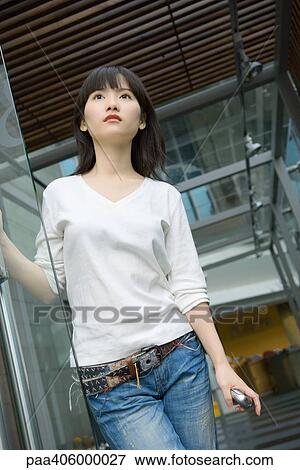Young woman standing in doorway, holding cell phone View Large Photo Image Stock Photo - Young woman standing in doorway, holding cell phone. Fotosearch
