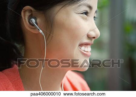 Stock Image - Young woman wearing earphones, smiling, close-up, profile. Fotosearch