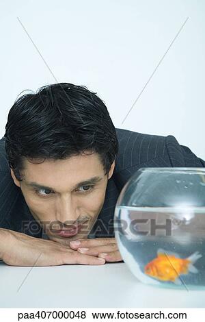 Stock Photo - Businessman looking at goldfish in fishbowl. Fotosearch