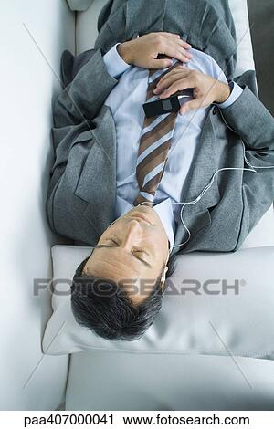 Stock Image - Businessman lying down, listening to earphones. Fotosearch