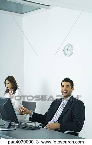 Stock Image - Businessman sitting at desk, holding yin yang balls. Fotosearch