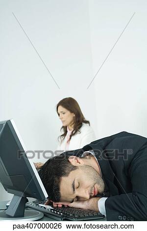 Businessman sleeping on keyboard while colleague works in background View Large Photo Image Stock Photograph - Businessman sleeping on keyboard while colleague works in background. Fotosearch