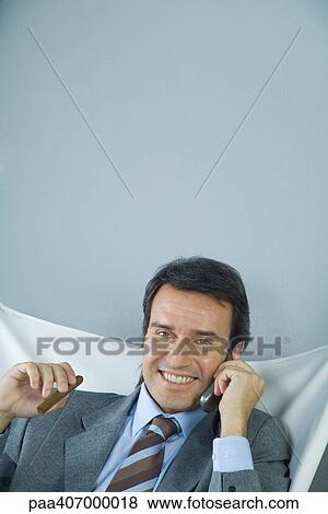 Businessman using cell phone and holding cigar, smiling at camera View Large Photo Image Stock Photo - Businessman using cell phone and holding cigar, smiling at camera. Fotosearch