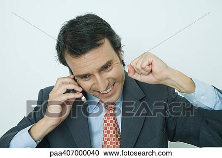 Businessman using cell phone, smiling, and making fist View Large Photo Image Stock Image - Businessman using cell phone, smiling, and making fist. Fotosearch