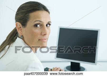 Businesswoman sitting at computer, looking over shoulder at camera View Large Photo Image Stock Photo - Businesswoman sitting at computer, looking over shoulder at camera. Fotosearch
